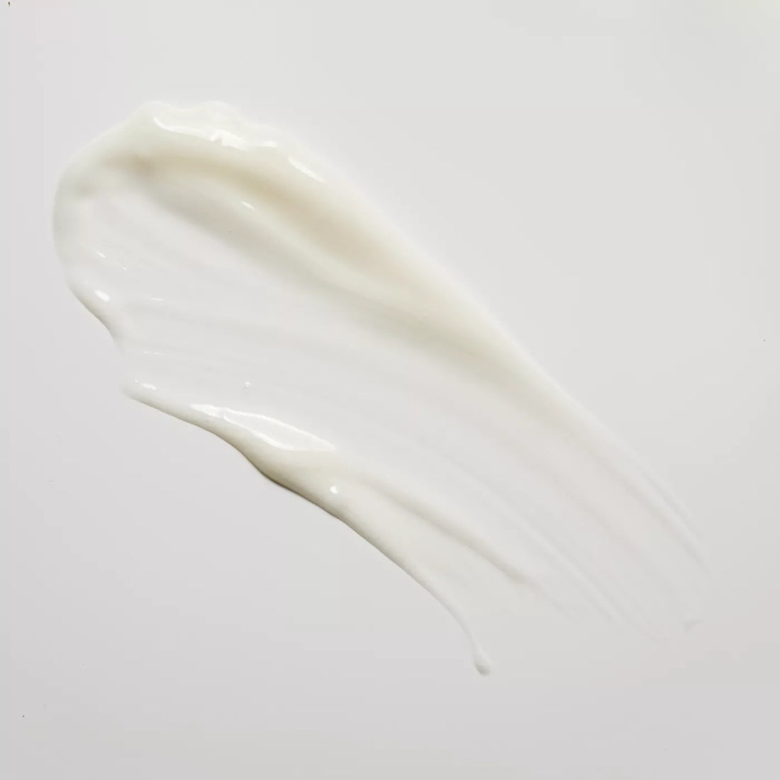 A thick, creamy white cosmetic smear on a plain light gray background.