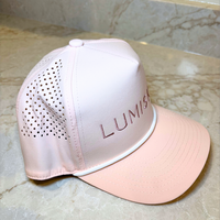 A light pink baseball cap with a matching curved brim, featuring a perforated mesh back panel and the brand name 'LUMISKIN'.