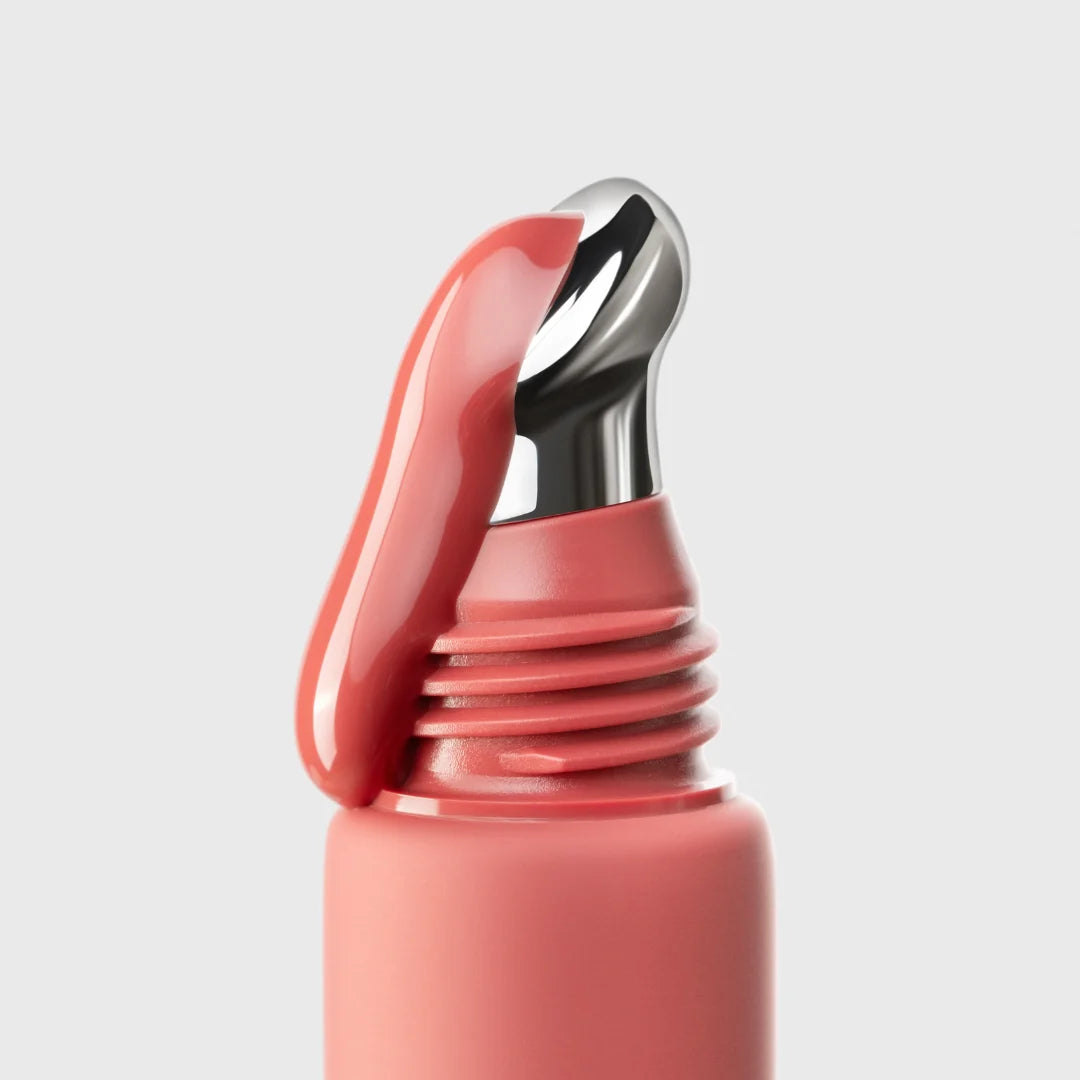 Close-up of a warm pink red lip gloss on a light gray background