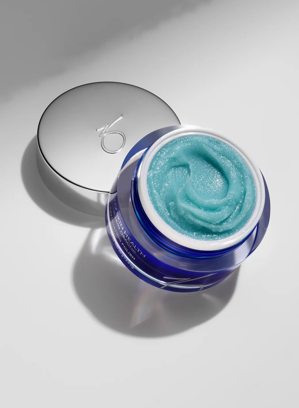 Blue polish in a jar with a silver lid on a light gray background