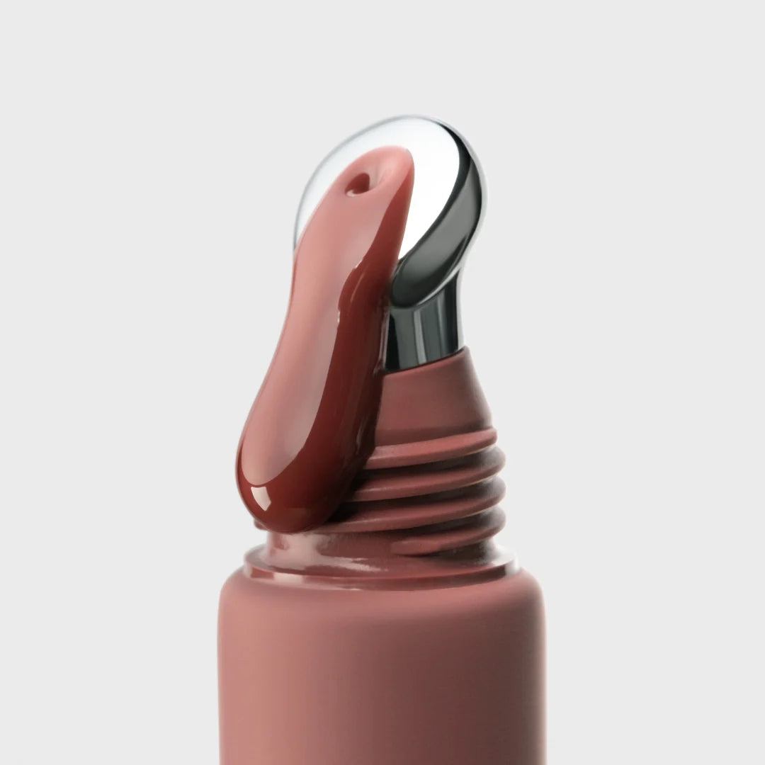 Close-up of a nude brown lip gloss with a silver applicator on a light gray background