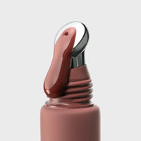 Close-up of a nude brown lip gloss with a silver applicator on a light gray background