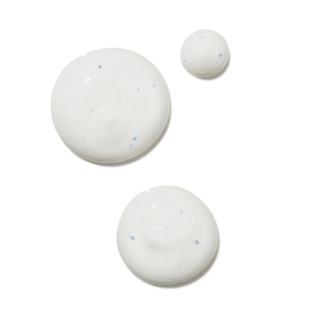 Three dollops of white serums with tiny blue specks, arranged on a plain white background.