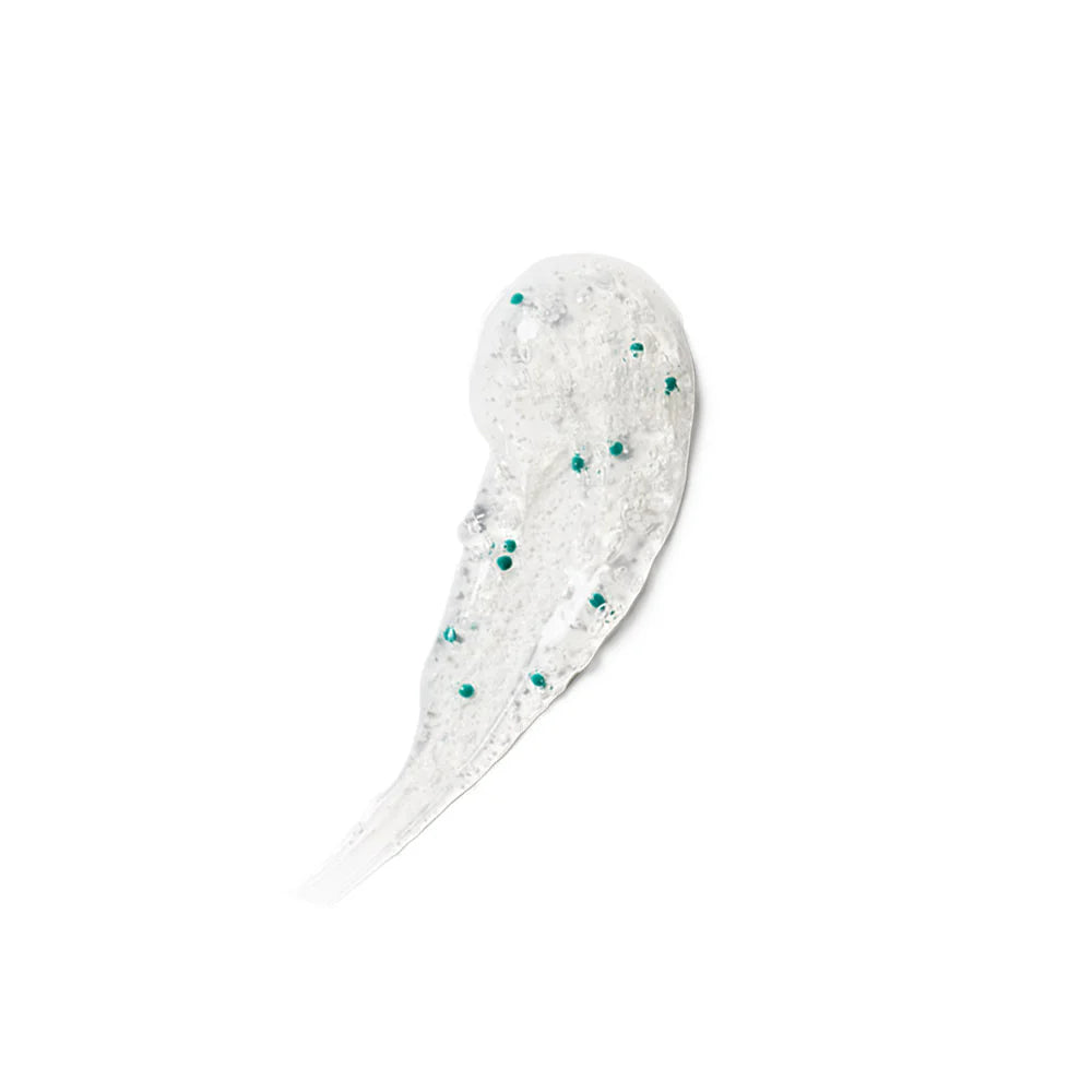 A smear of clear gel scattered small teal-green exfoliating beads on a plain white background.