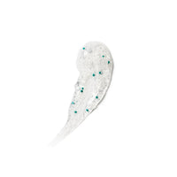 A smear of clear gel scattered small teal-green exfoliating beads on a plain white background.