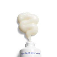 A thick, creamy off-white cream is shown squirting from a white squeeze tube against a solid white background.